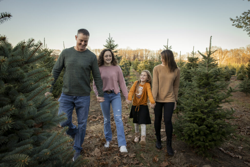 family of four walks towards camera holding hands at christmas tree farm in dexter michigan