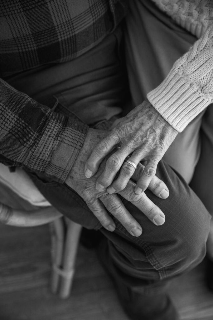 black and white photo of close up of elderly couple's hands on husband's lap