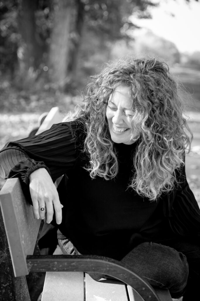 Black and white photo of woman laughing and sitting on bench in park