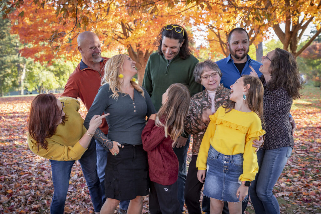 large family laughs together among bright orange fall leaves