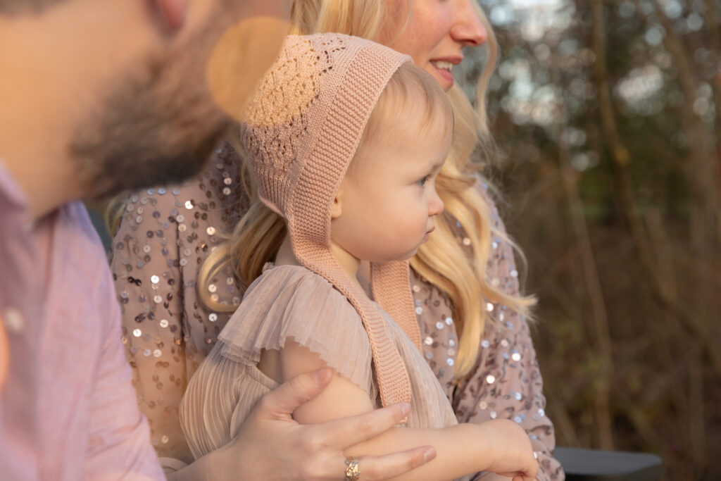 A young toddler girl sits on the lap of her mother outside and looks off to the right of frame.