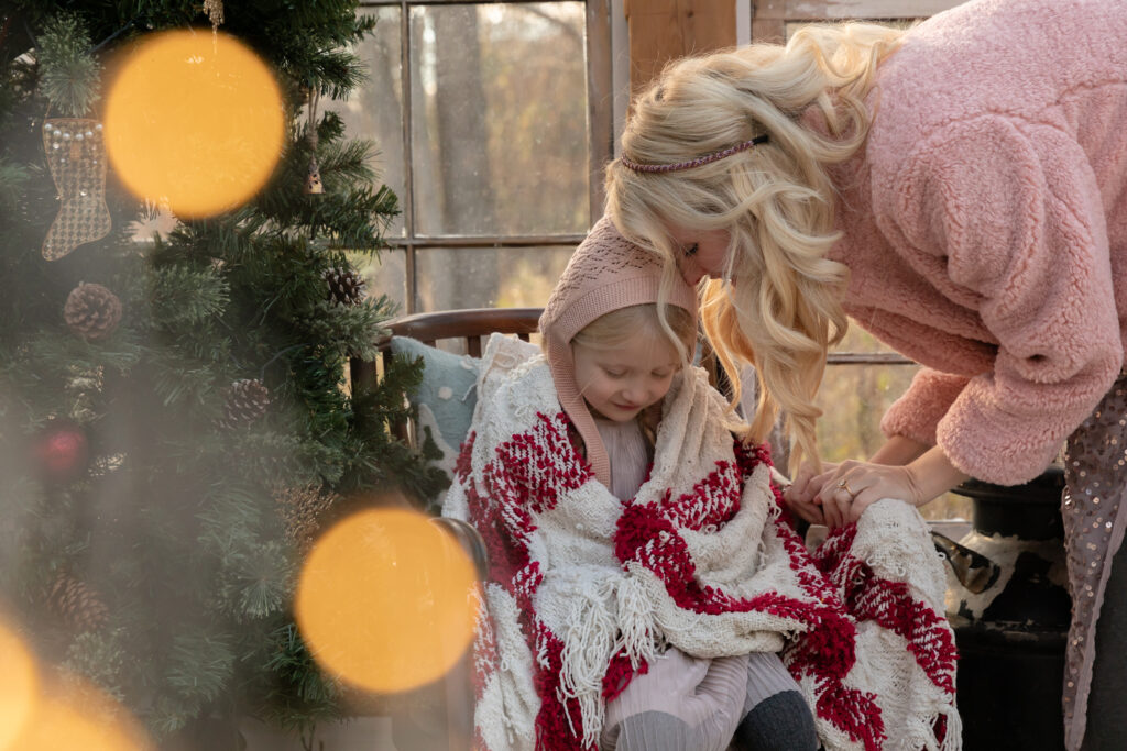 A mother leans down to snuggle with her daughter in a greenhouse decorated for Christmas