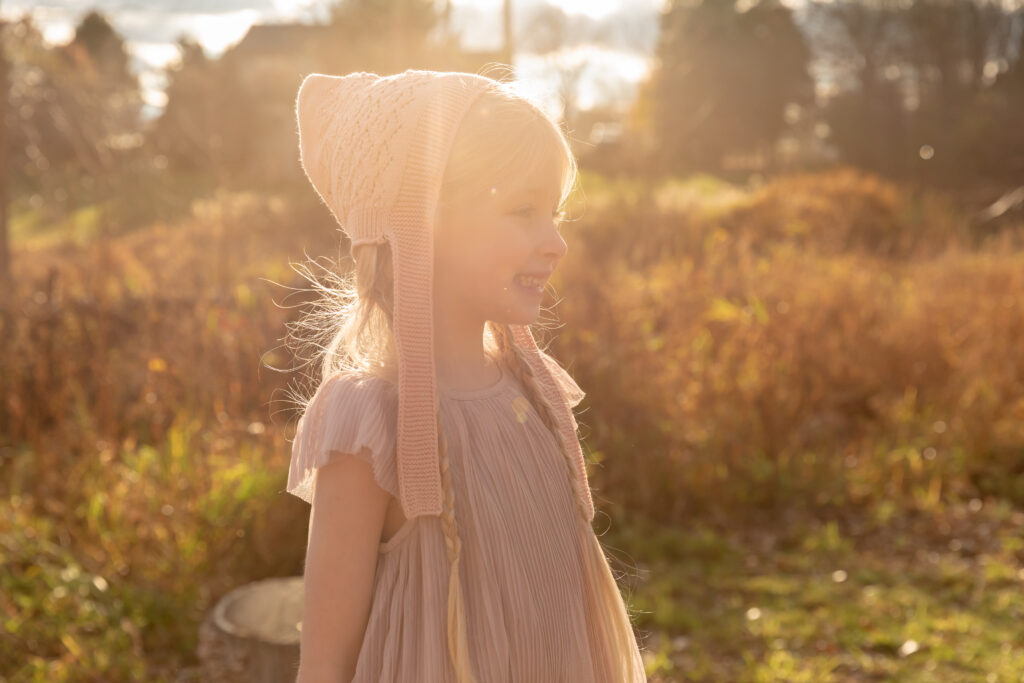 Young girl stands staring off camera with a big smile and sun behind her in a field of dormant wildflowers and grasses