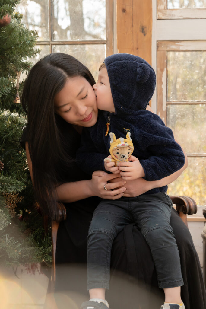 Young boy kisses his mother on the cheek in a greenhouse decorated for christmas