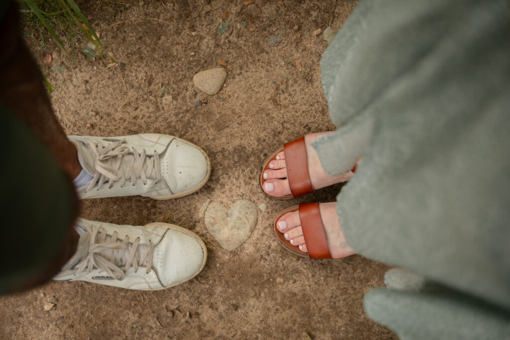 heart rock on path photo taken from above of mother and father standing on either side of the rock during maternity photos at Saginaw Forest in Ann Arbor, Michigan