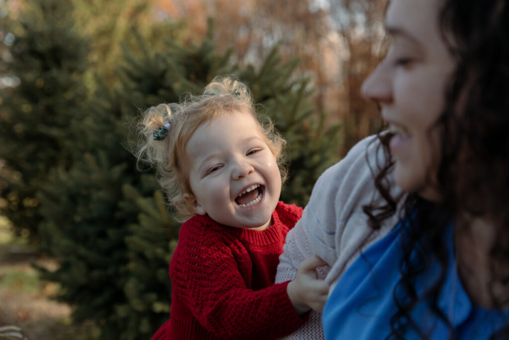 toddler girl laughs and tickles mother in tree form mini session at westmans tree farm in dexter michigan