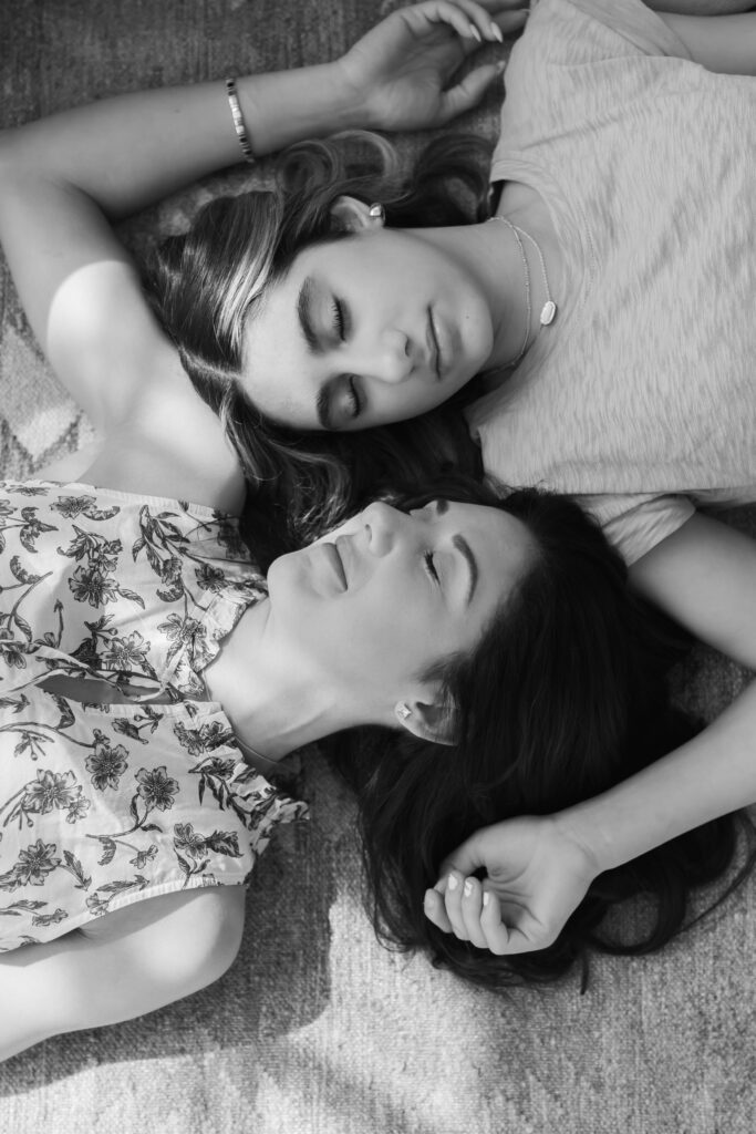 mother and teenage daughter lay on the floor in a black and white image with photo captured from directly above as they each lay different directions and we see their eyes closed and heads near each other at studiostudio motherhood session in ann arbor