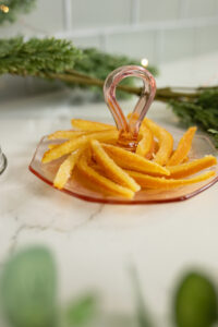 candied orange peels on pink vintage plate with christmas greenery and twinkle lights