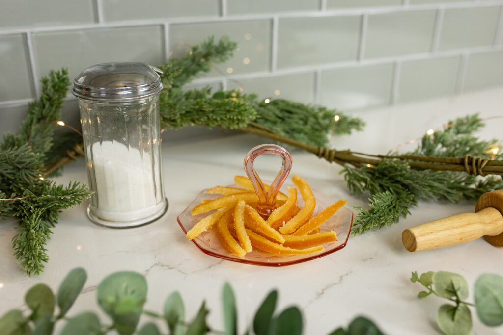 candied orange peels on pink vintage plate with christmas greenery and twinkle lights and sugar shaker