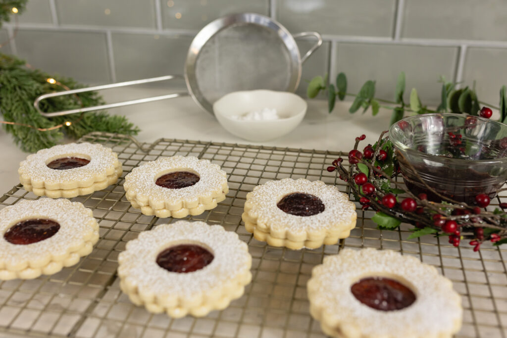 Linzer cookies on rack with raspberry jam and christmas decor around