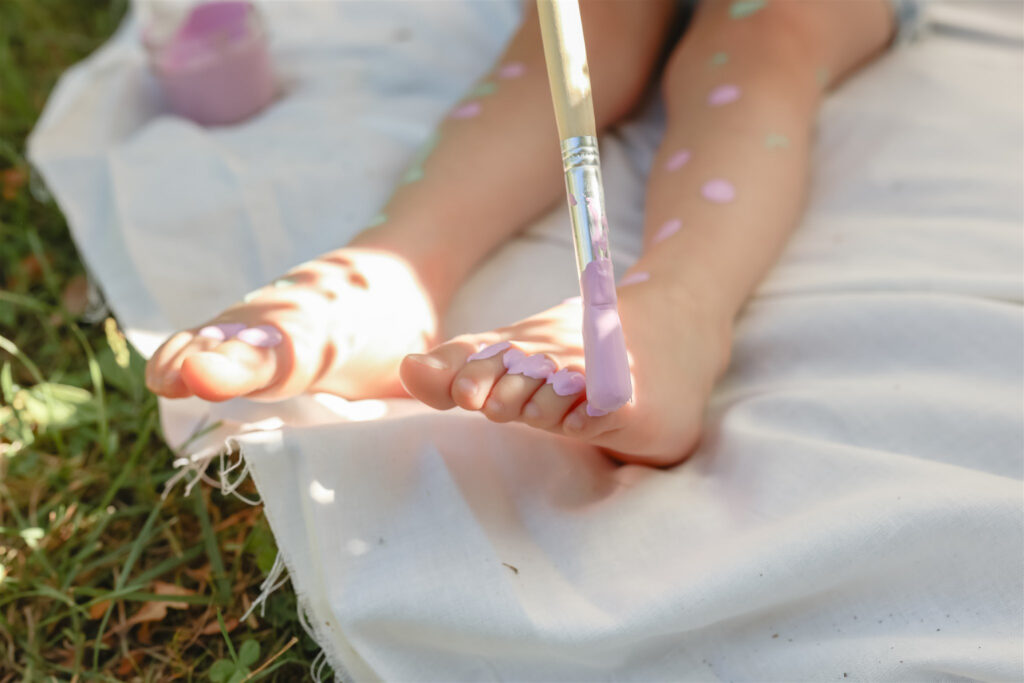 young girl paints her toes and feet lavender in this detail shot from a mother daughter paint party photoshoot in saline michigan