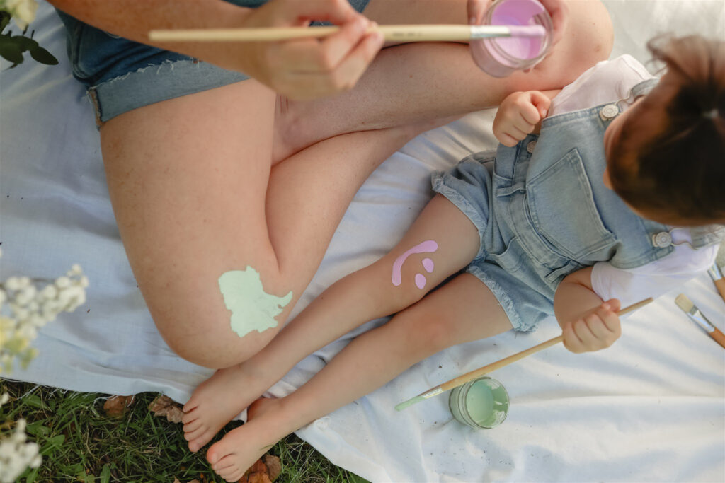 detail shot from above of a girl with her mother who are painting smiley faces and spots on each other's legs during a paint party photoshoot in saline michigan