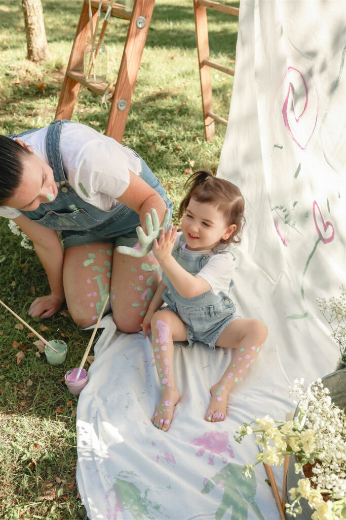 mother and daughter give each other a high five with paint covered hands during a mother daughter paint party photoshoot at a park in saline michigan