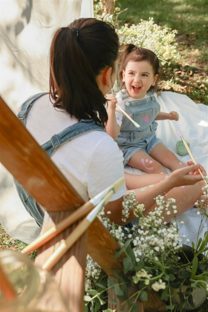 girl looks up to mother and smiles during mother daughter paint party photoshoot surrounded by flowers and paint supplies