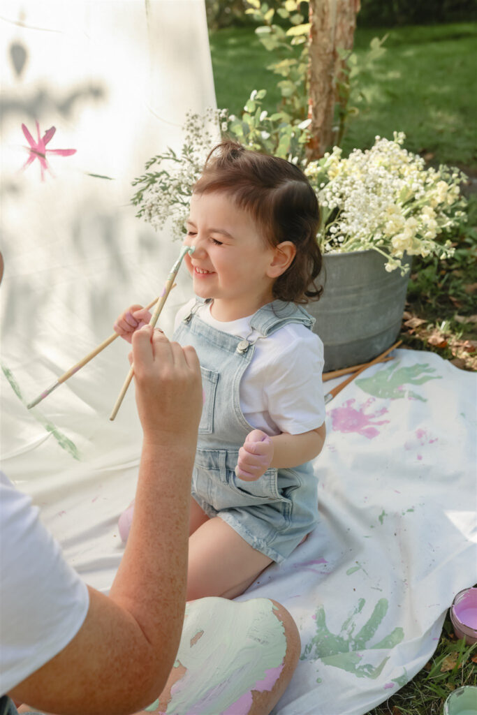 mother paints daughter's nose while daughter smiles with eyes closed during mother daughter paint party photoshoot