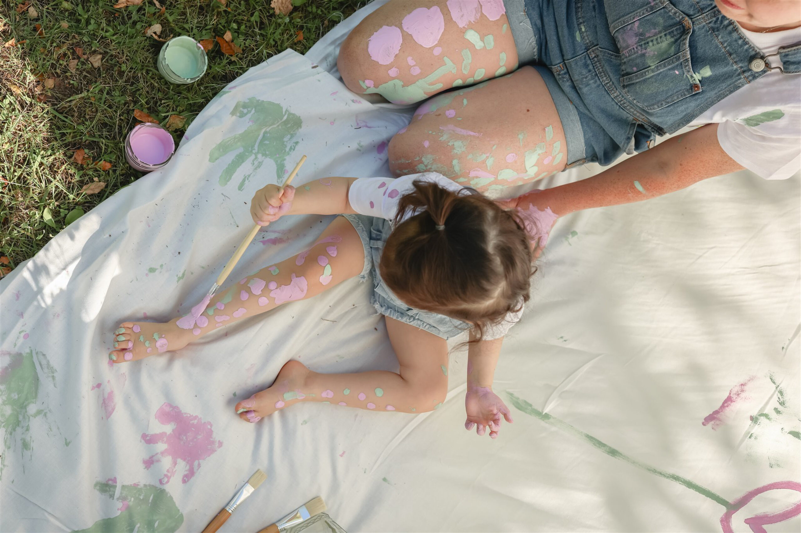 top down photo of a young girl painting on her leg during a mother daughter paint party photoshoot in saline michigan