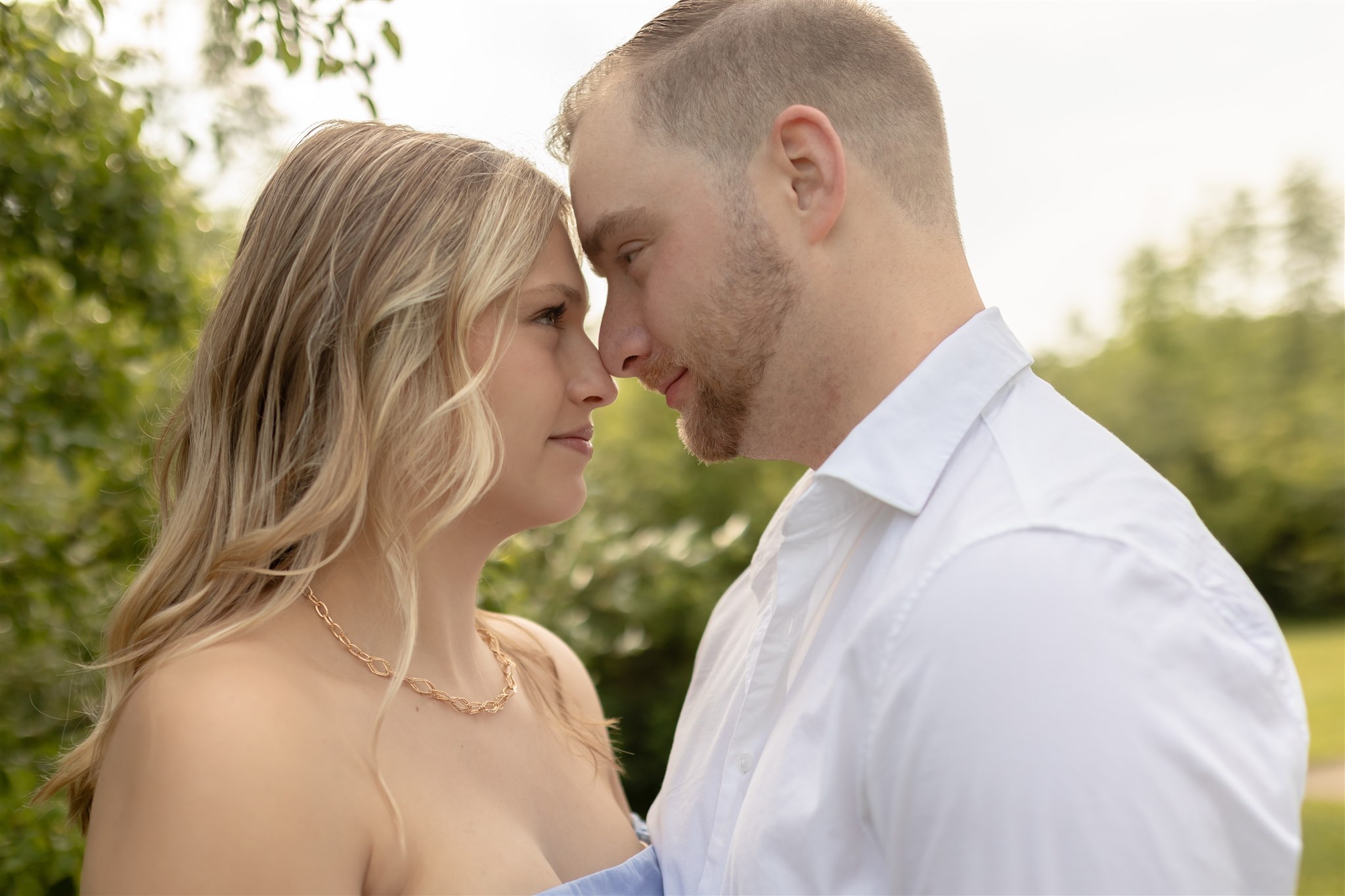 Couple stares into each other's eyes and smile while leaning in for a nose touch in a park