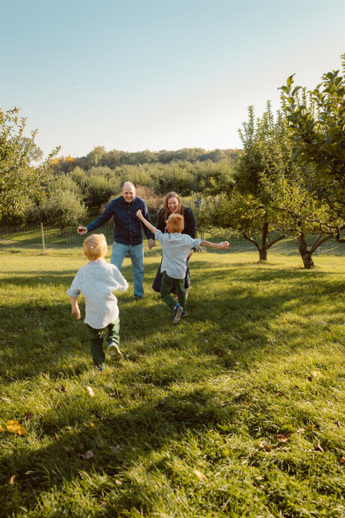 young boys run away from camera towards their parents in between rows of apple trees at alber orchard in manchester michigan