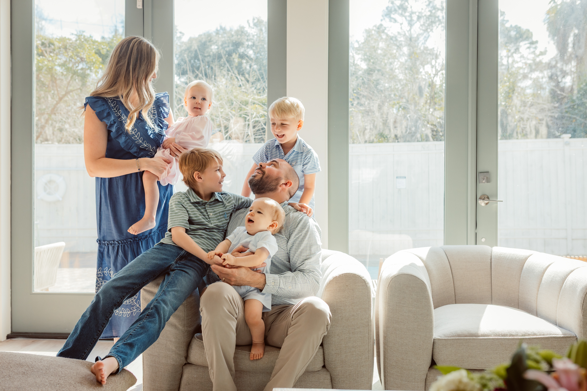 Bright and joyful in-home family photography session by an Ann Arbor family photographer, capturing parents with their four young children laughing and cuddling together in a sunlit living room