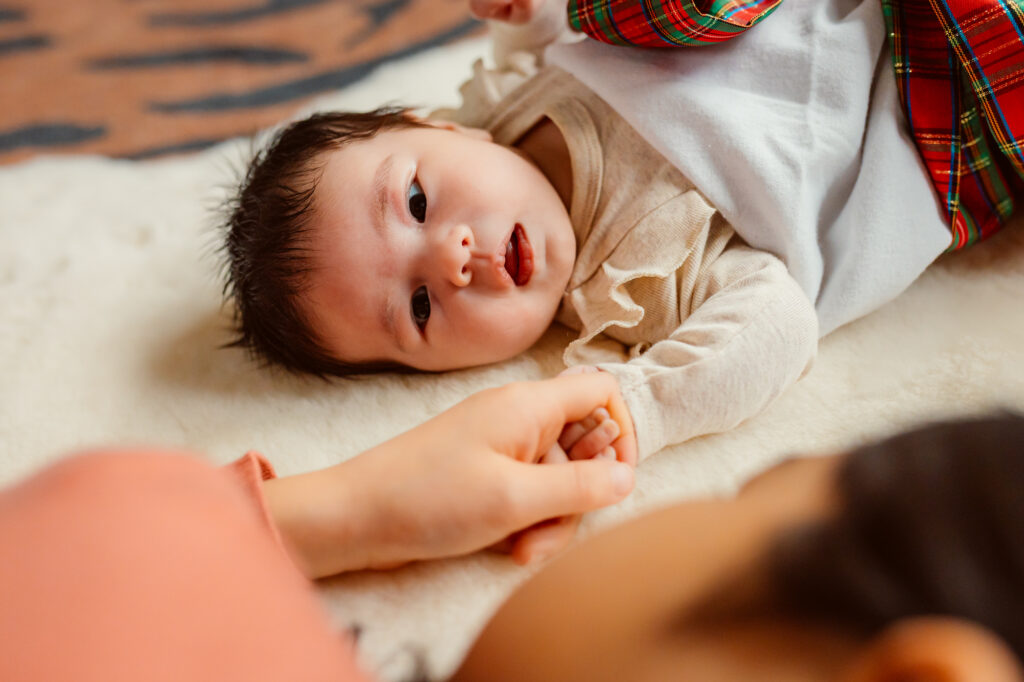 An older sibling gently holds a newborn’s tiny hand during an in-home newborn photo session in Ann Arbor, Michigan, highlighting sibling connection and early family moments captured by a Michigan newborn photographer.
