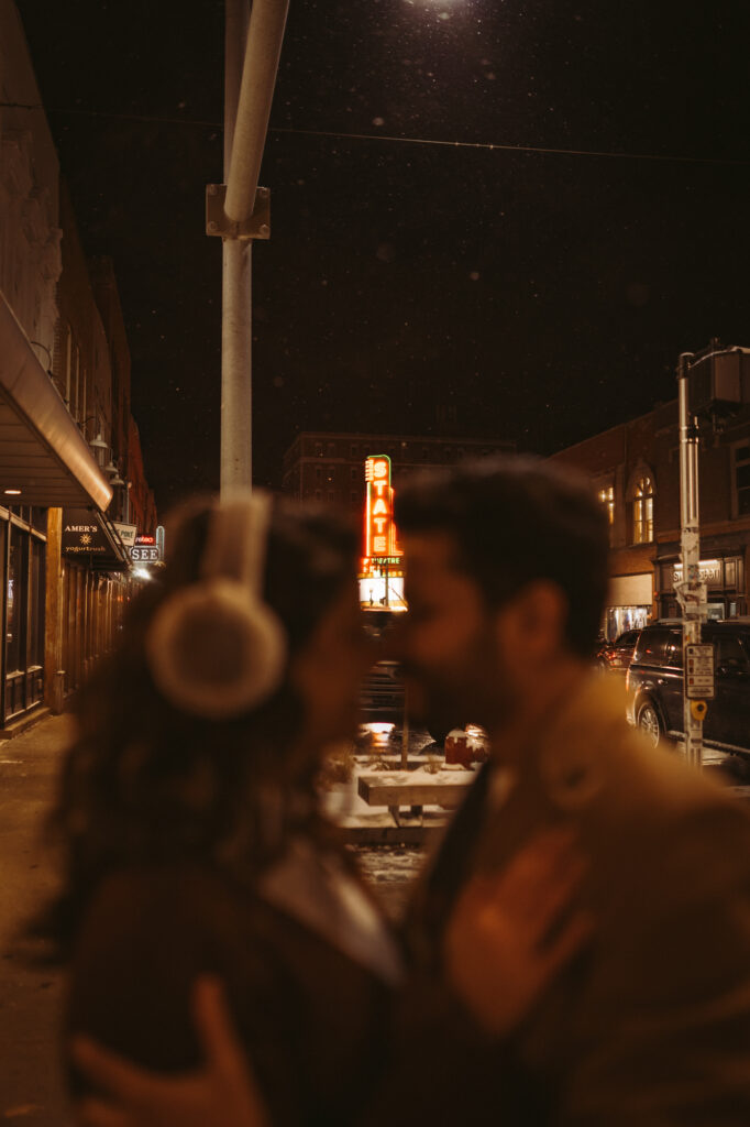 Man and woman touch noses with the state theater marquee in focus between their faces