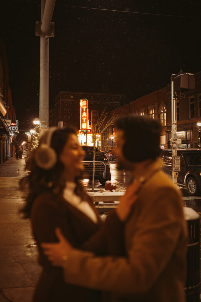 Man and woman look at each other while embracing, and the state theater marquee is in focus behind them