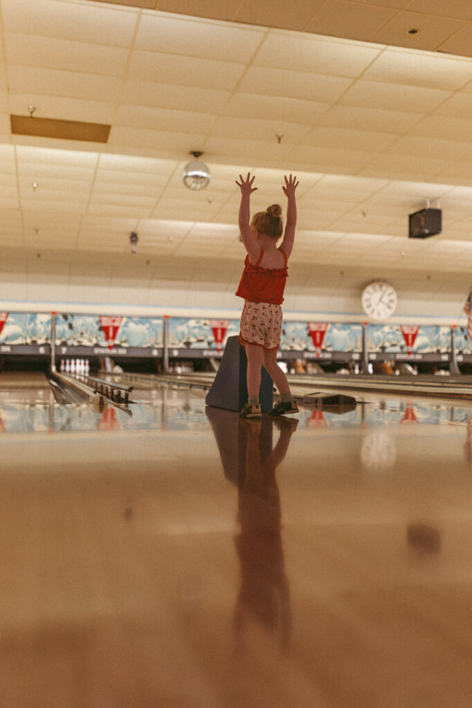 girl throws her arms up after sending bowling ball down the alley while playing bumper bowling