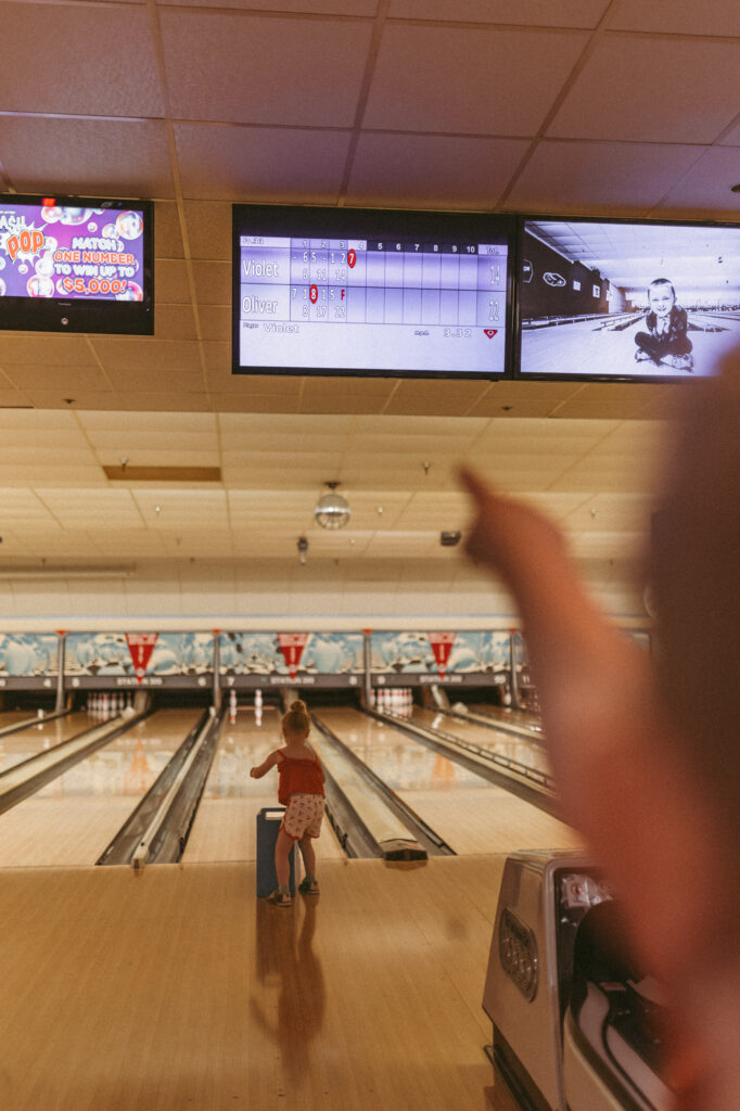 boy points to bowling score while girl bowls a frame