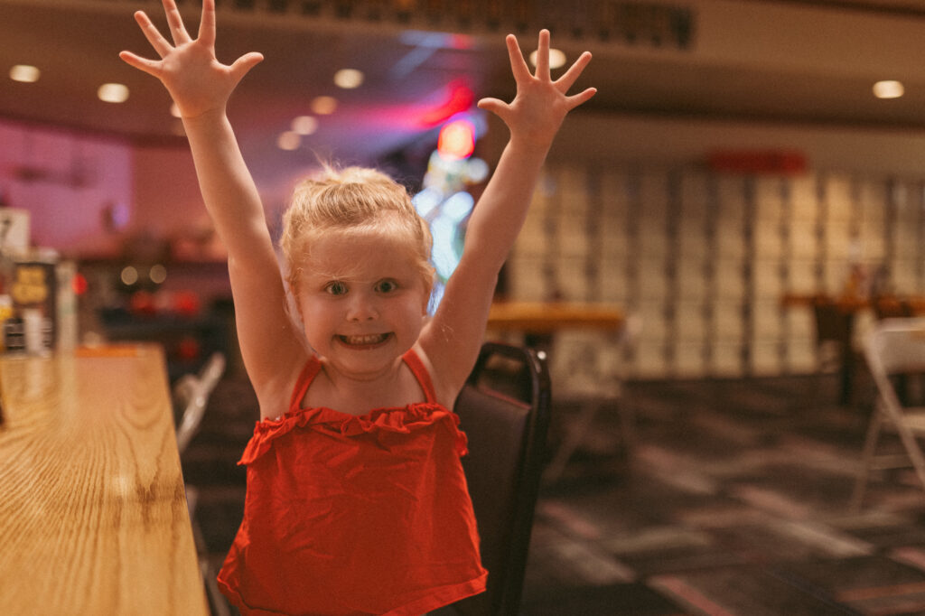girl holds arms up high and smiles at station 300 bowling alley in saline michigan