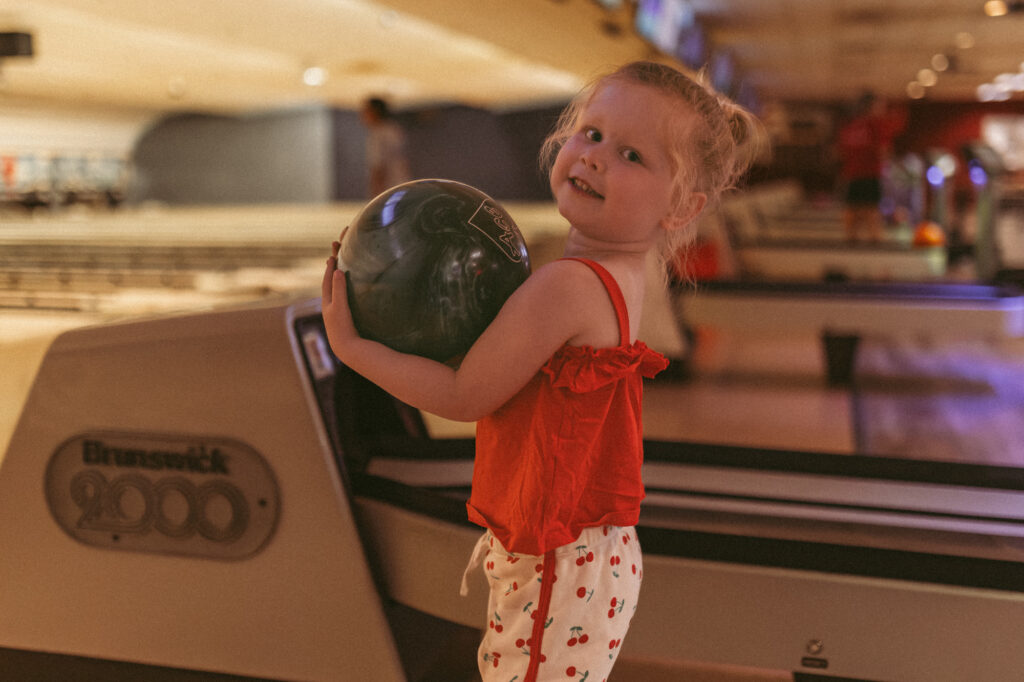 young girl holds bowling ball while standing next to ball return machine at station 300 in saline michigan