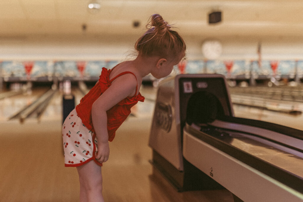 girl peeks into ball return at bowling alley waiting for ball to return