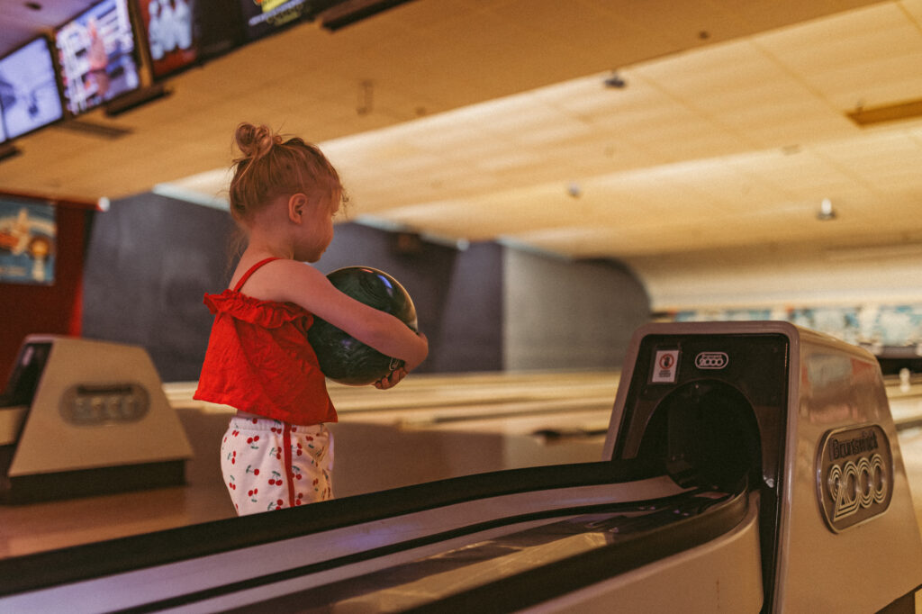 young girl holds bowling ball in her arms waiting to roll her ball down the lane